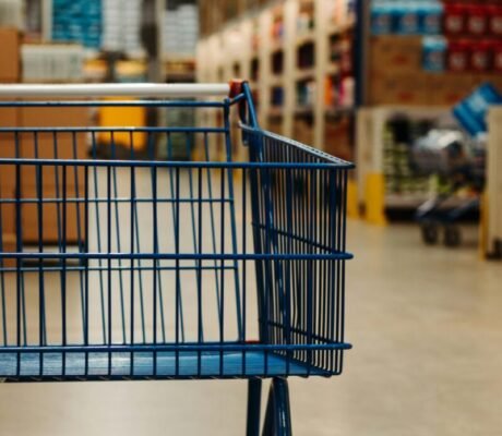 Side view of an empty shopping cart in a warehouse supermarket aisle with blurred merchandise.